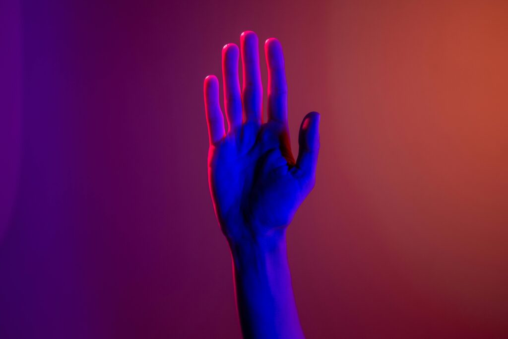 Raised hand illuminated with colorful lighting symbolizing support, help, and community awareness.